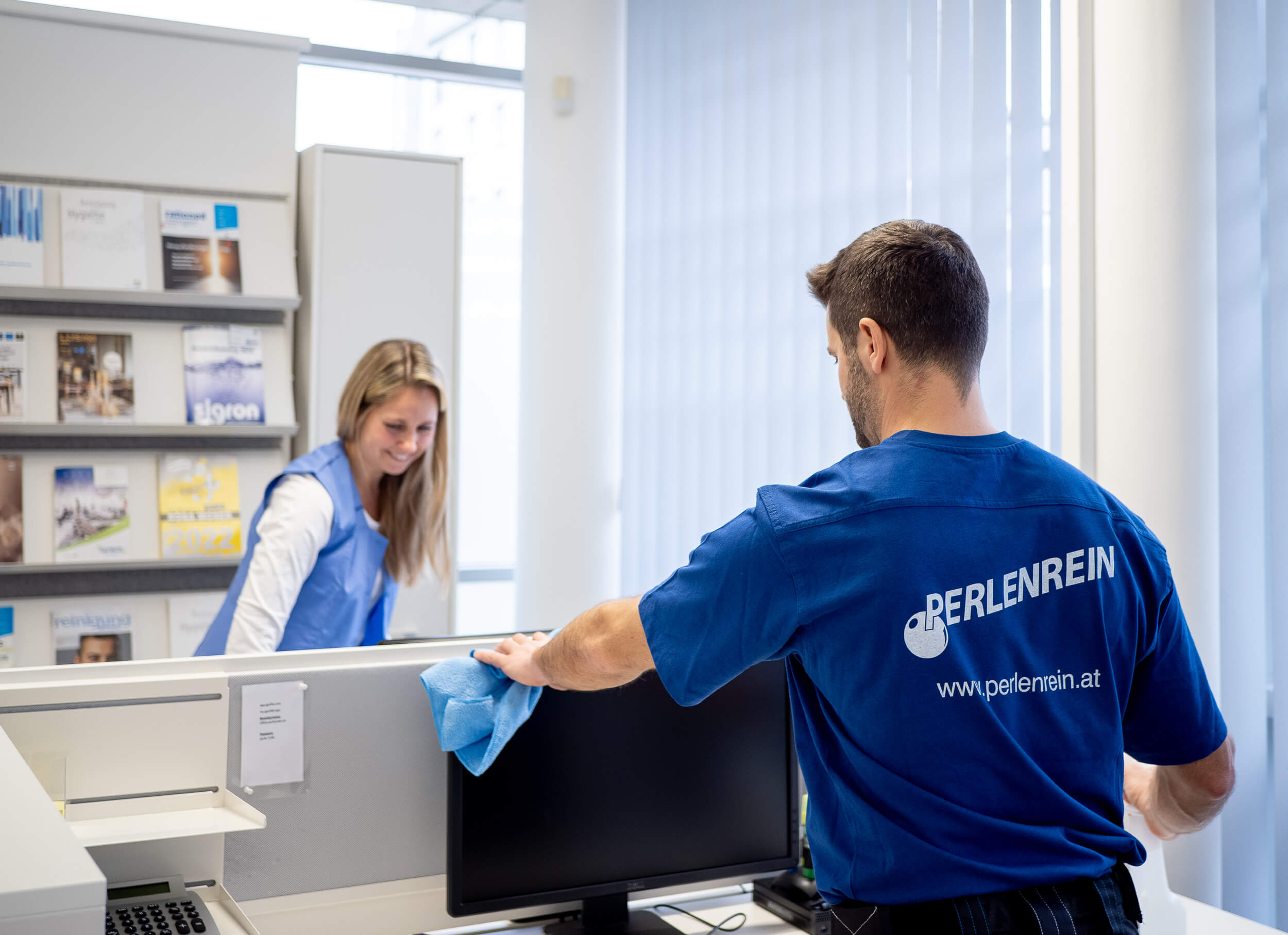 Perlenrein-Mitarbeiter reinigt einen Schreibtisch im Rahmen der laufenden Unterhaltsreinigung im Büro