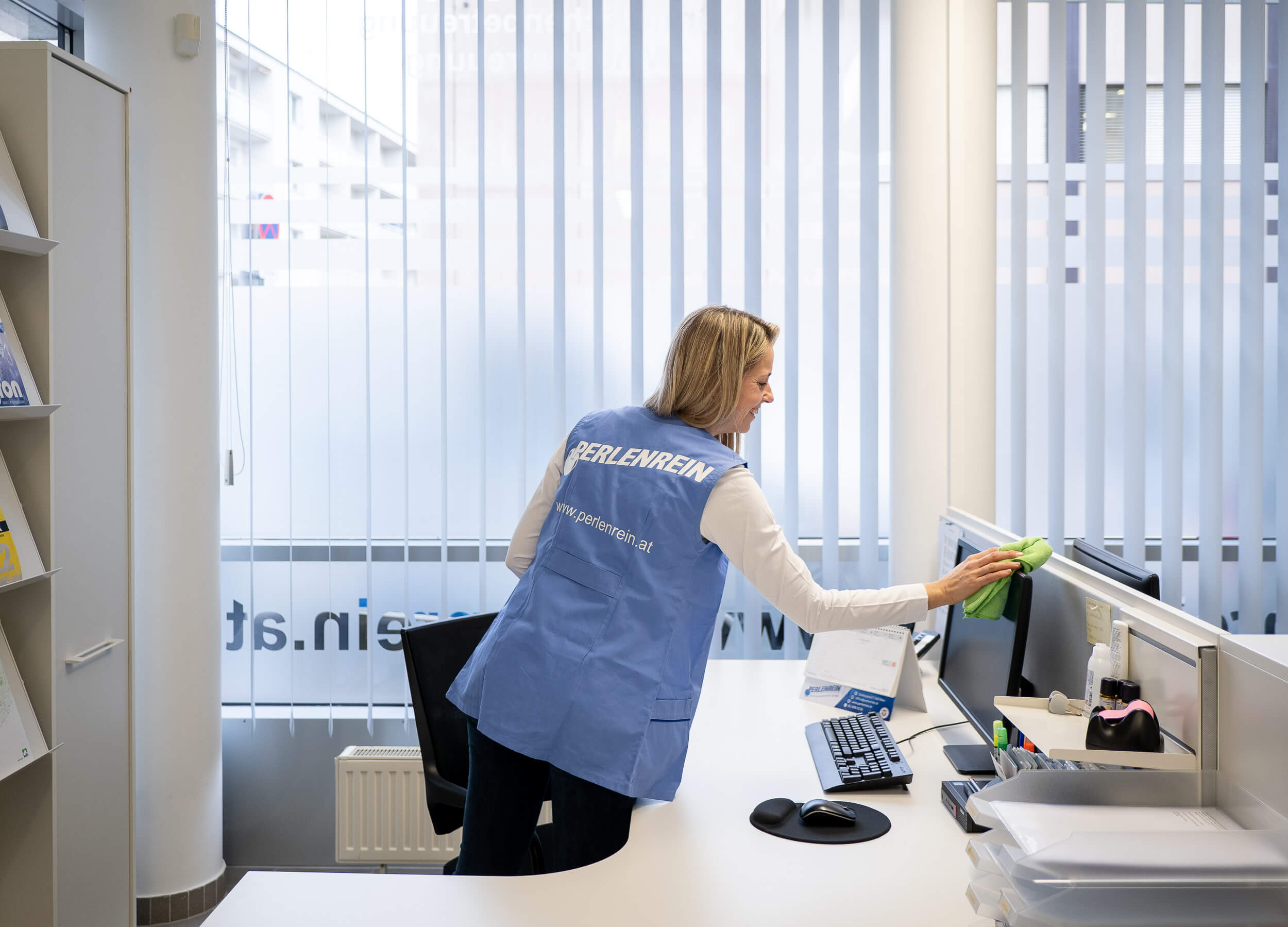 Perlenrein-Mitarbeiterin reinigt einen Bildschirm am Büroarbeitsplatz mit einem Mikrofasertuch